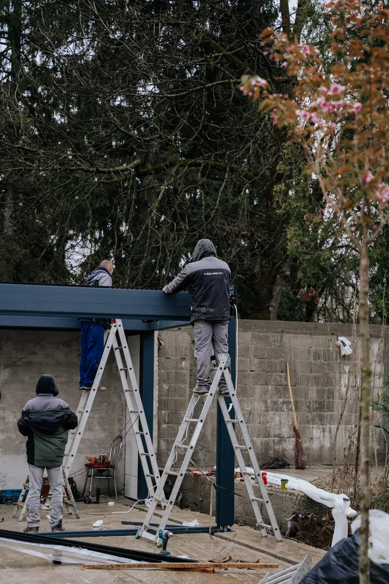 Doi montatori HEXANN pe scări ridică structura unei pergole bio-retractabile în Cluj