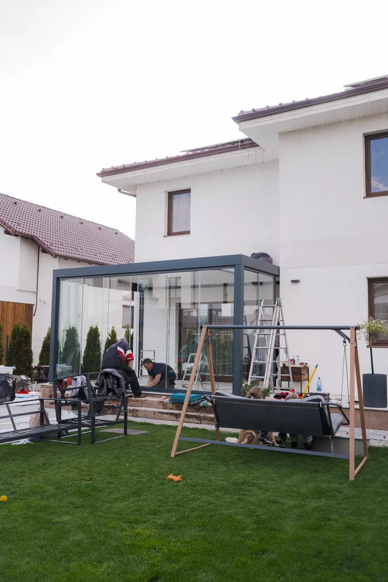 Pergolă bioclimatică HEXANN cu sticlă la o casă albă din Mediaș, văzută din grădină