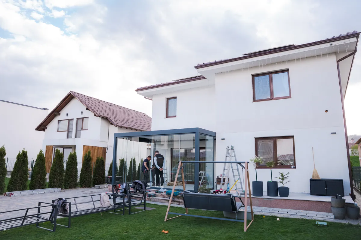 Casă albă din Mediaș cu pergolă bioclimatică HEXANN și închidere din sticlă la terasă