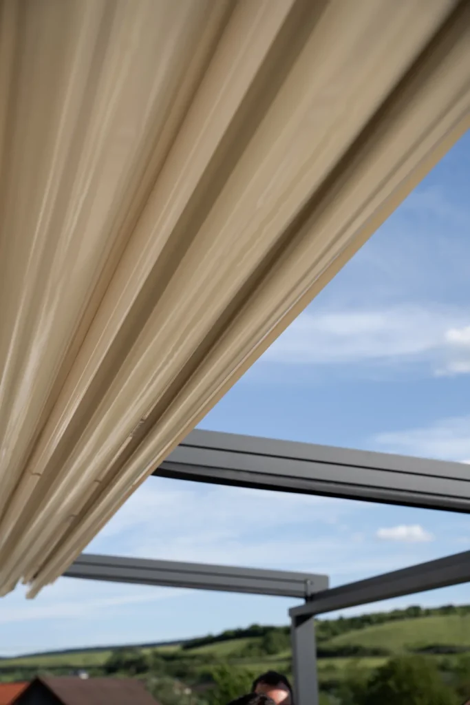 Membrana PVC întinsă a pergolei retractabile din Cluj, văzută de jos, cu cer și nori