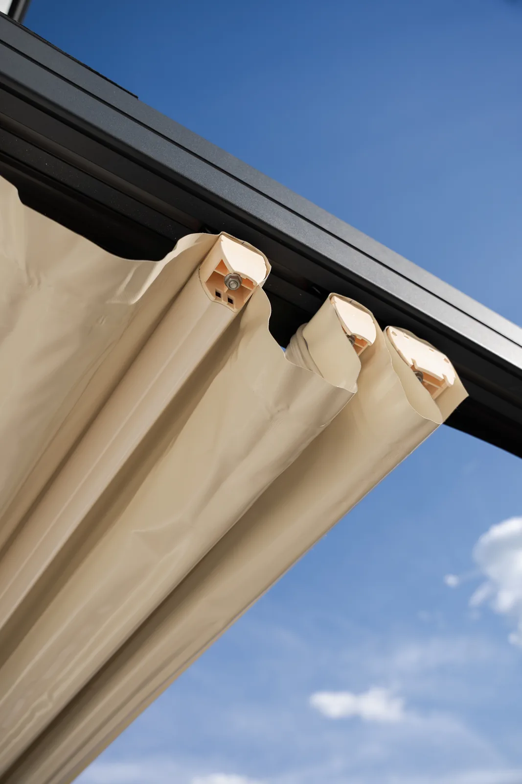 Membrana PVC parțial întinsă pe structura antracit a pergolei din Cluj, cu cer albastru