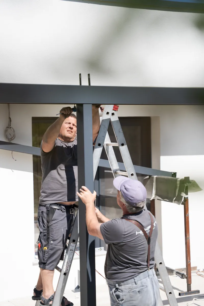 Doi montatori HEXANN fixează stâlpul pergolei retractabile PVC la casa din Cluj